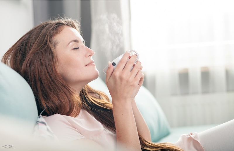 Young woman sitting on couch at home and drinking coffee, casual style indoor shoot